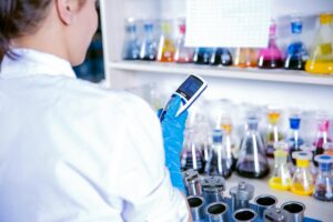 Scientist using a device to analyze chemical samples in a lab setting with colorful beakers.