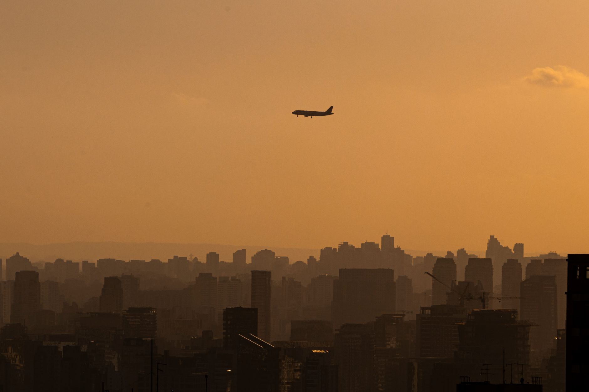 A silhouette of an airplane flying over Sao Paulo's skyline during a golden sunset.