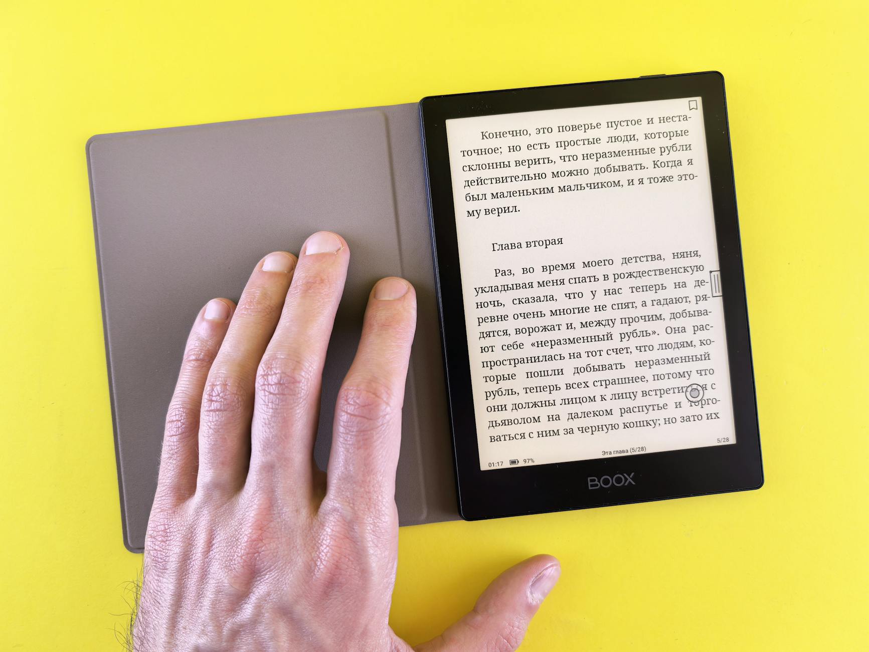 A hand holding an e-reader displaying text on a bright yellow background, showcasing modern digital reading.