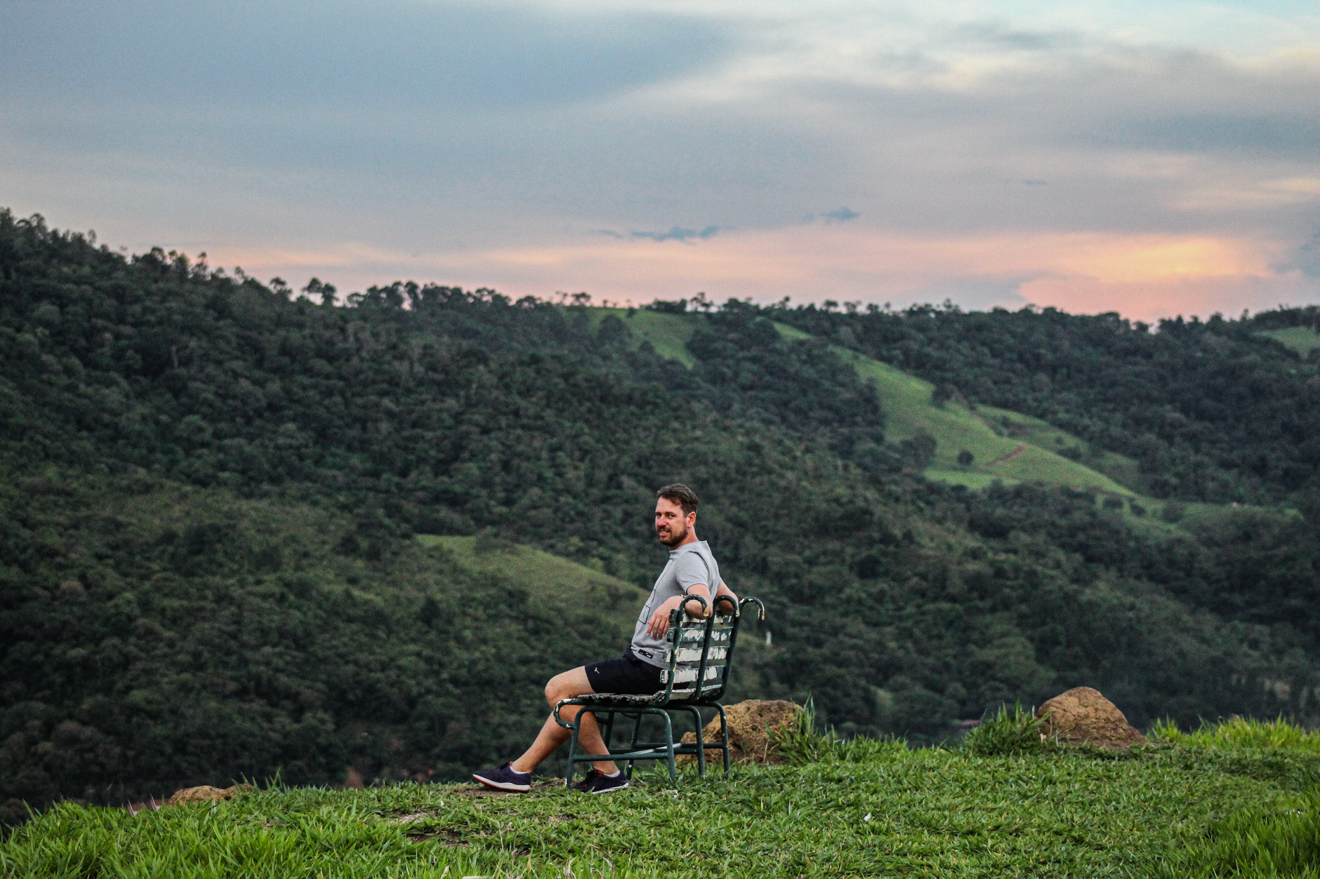 A man sits on a bench enjoying a serene view of a lush green valley at sunset.