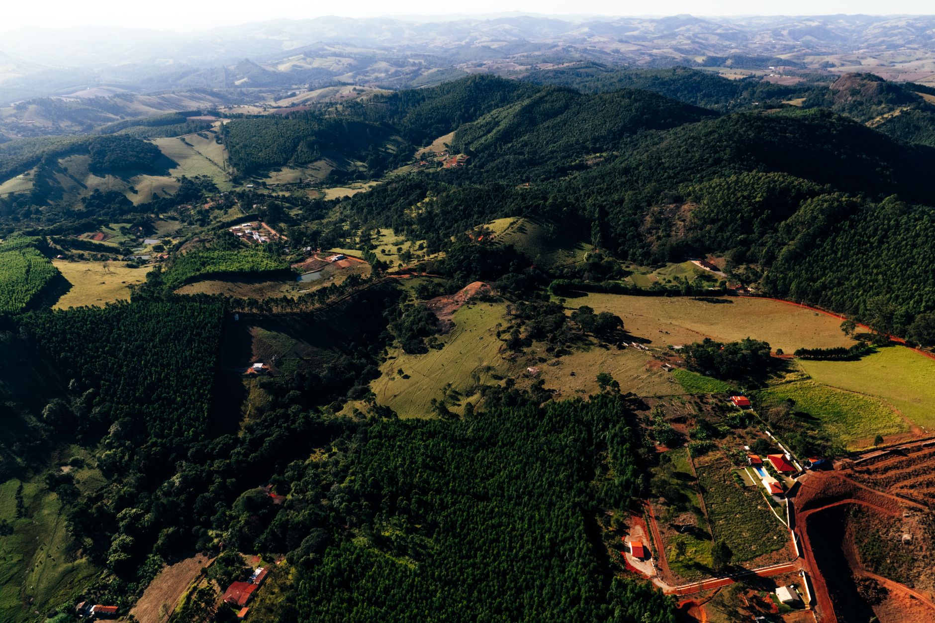 From above of picturesque landscape of lush mountains and high hills with small settlement in grassy valley surrounded by forest