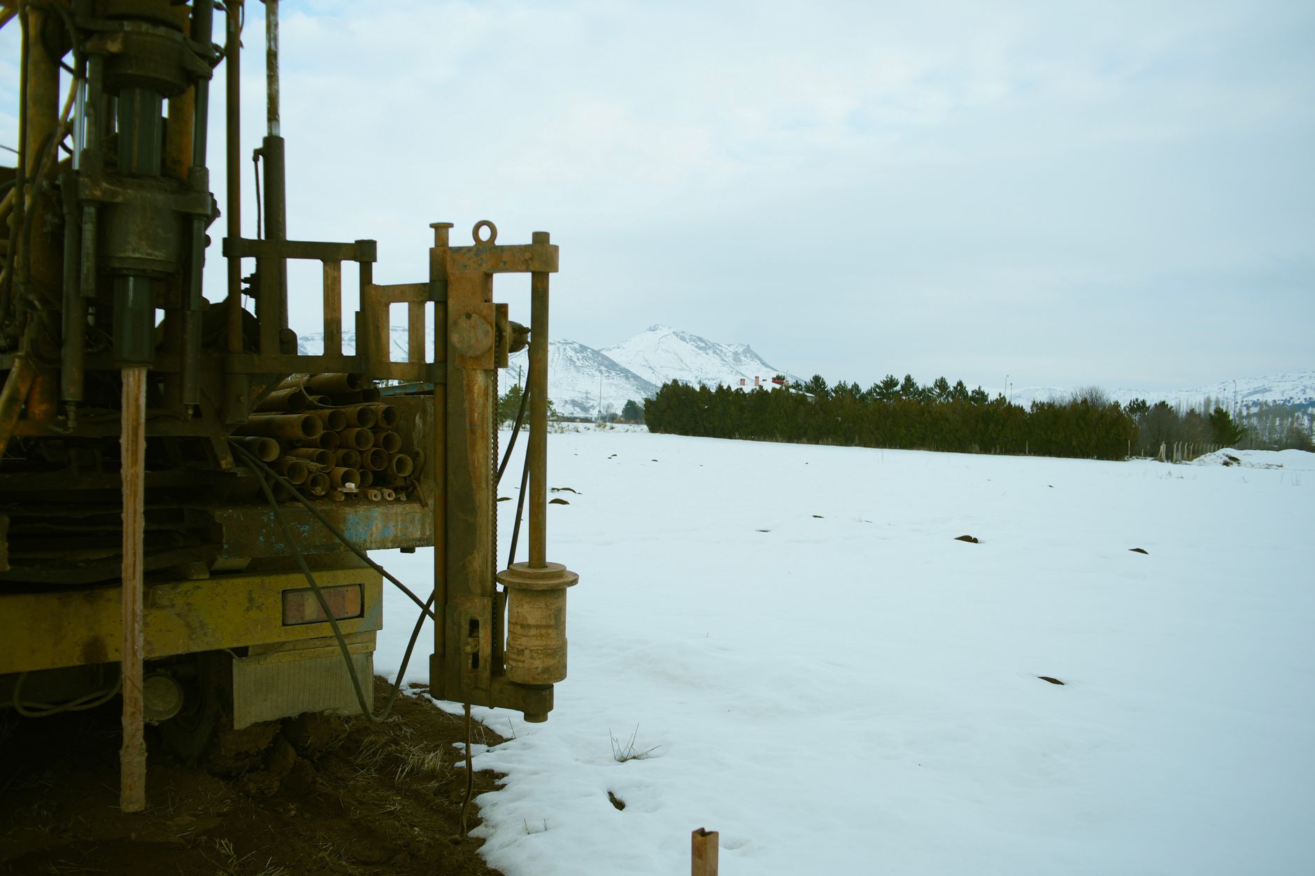 A large industrial drill machine set against a snowy winter landscape with mountains in the background.