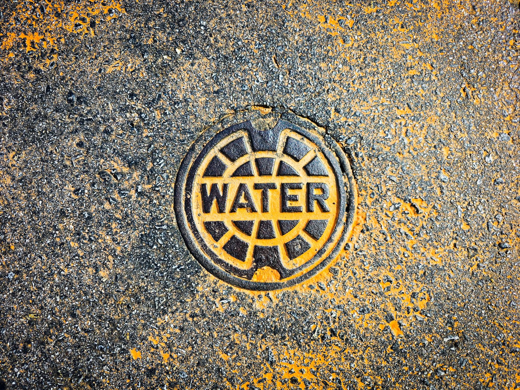 Colorful water utility cover on street pavement blends art with functionality.