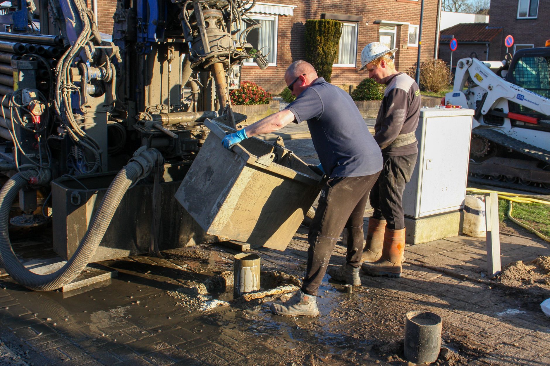 Workers operating drilling machinery on a construction site, managing equipment outdoors.
