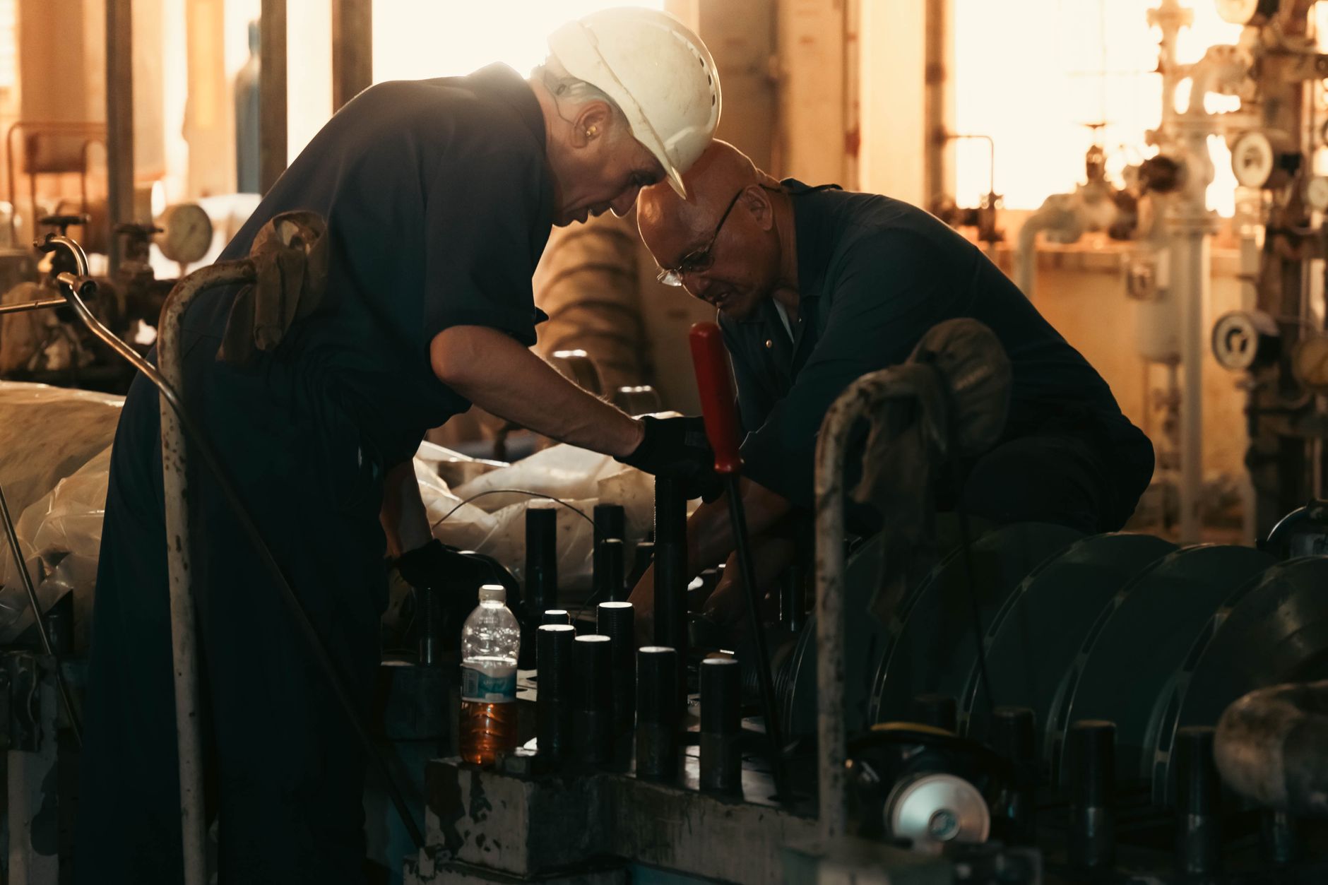 Two engineers collaborating on machinery maintenance in a dimly lit industrial plant.