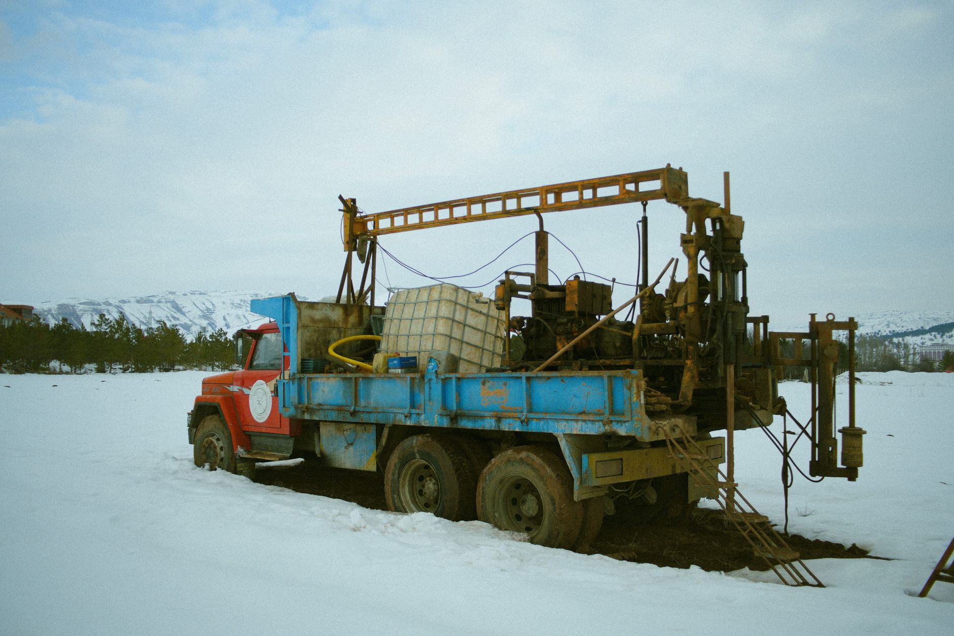 Rustic vintage truck with equipment on a snowy field under a cloudy winter sky.