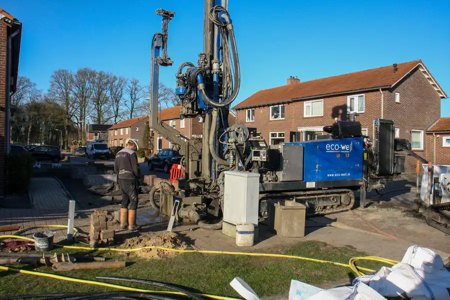 Construction site with worker and drilling machine operating near residential area on a sunny day.