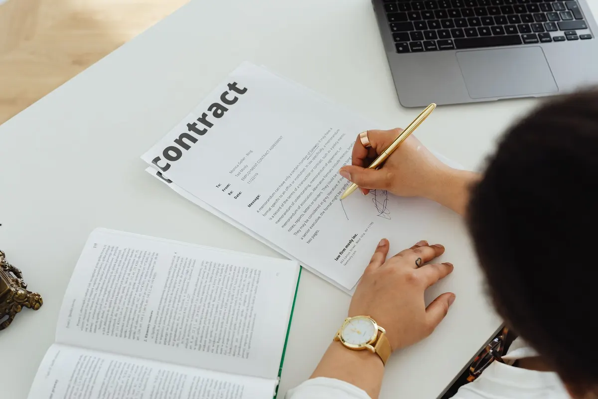 Professional signing a business contract at a modern desk setup for office work.