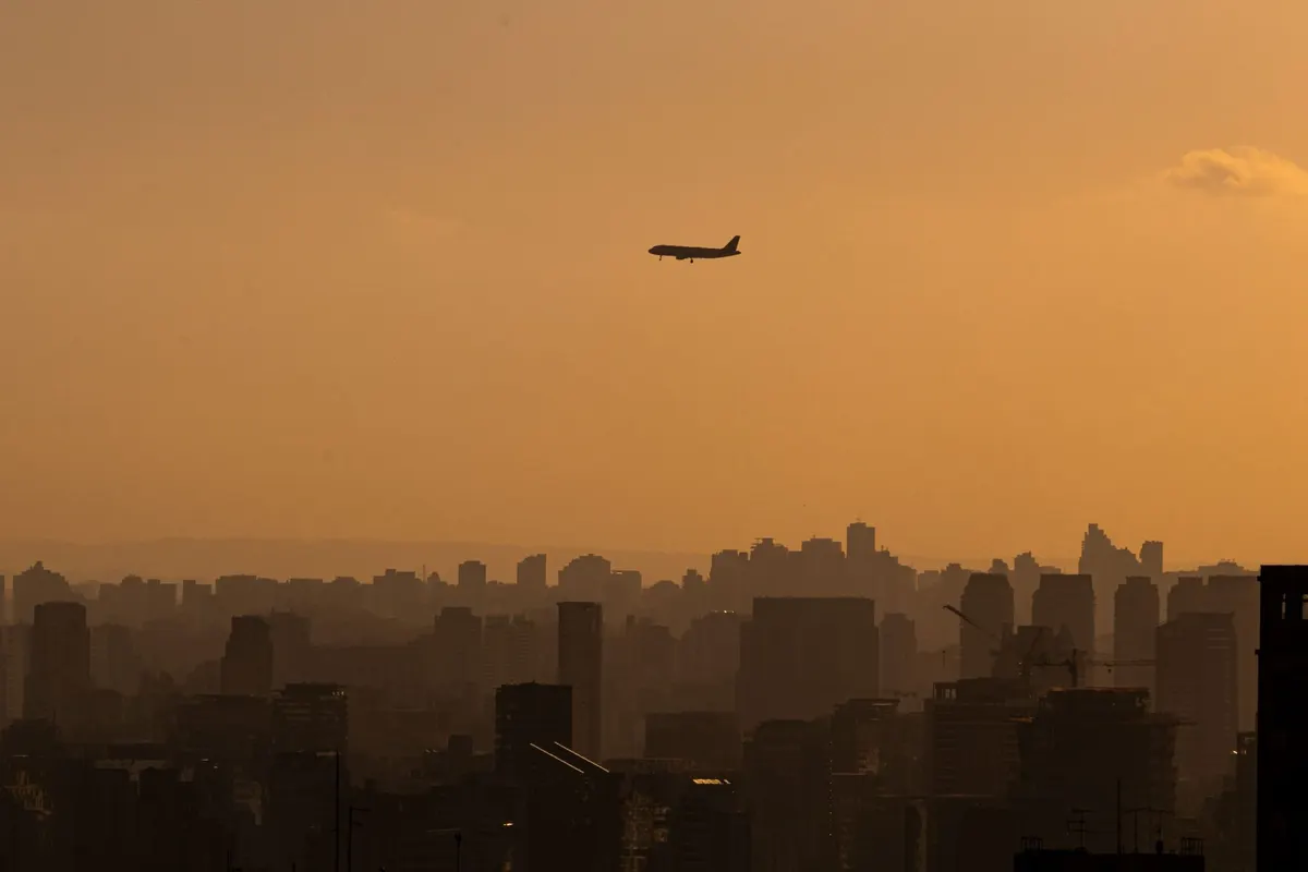 A silhouette of an airplane flying over Sao Paulo's skyline during a golden sunset.