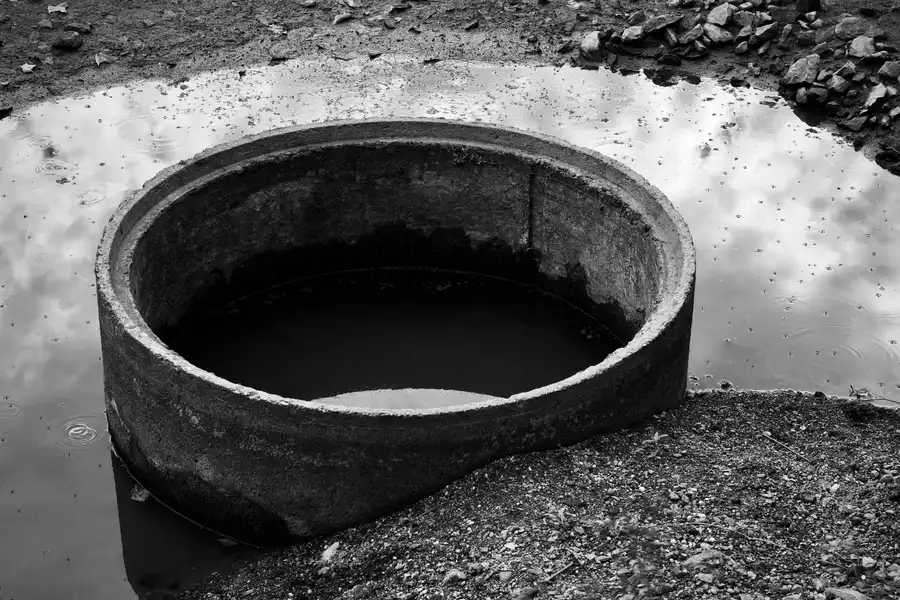 Circular concrete structure in puddle reflects sky in monochrome.